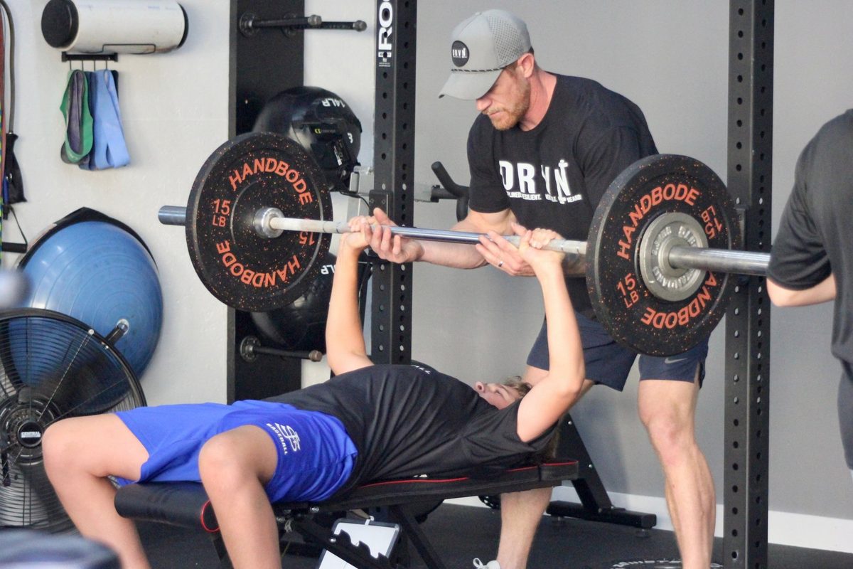 Coach Brandon spotting a young athlete on the bench press